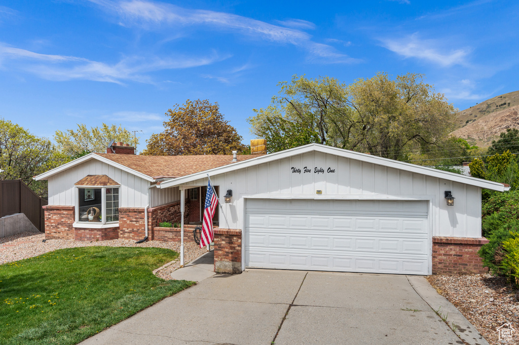 Ranch-style home with a front lawn, brick siding, a garage, a chimney, and concrete driveway