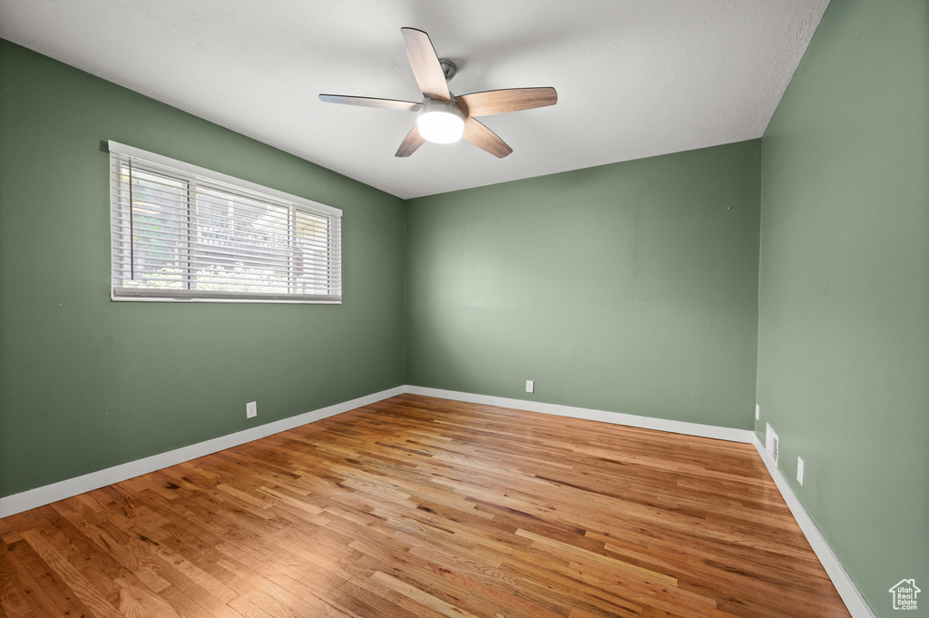 Empty room with a ceiling fan, wood finished floors, and baseboards