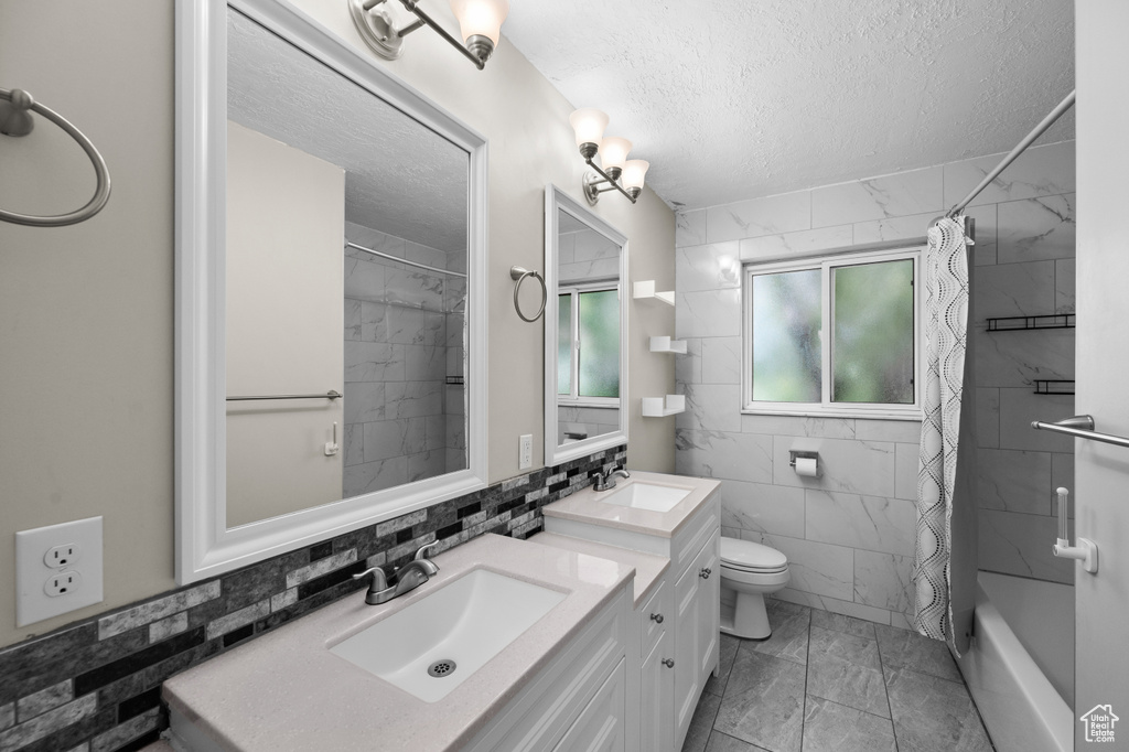 Bathroom featuring marble finish floors, a textured ceiling, tile walls, toilet, and double vanity