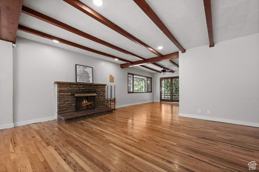 Unfurnished living room featuring a ceiling fan, light wood-style floors, beam ceiling, a fireplace, and recessed lighting