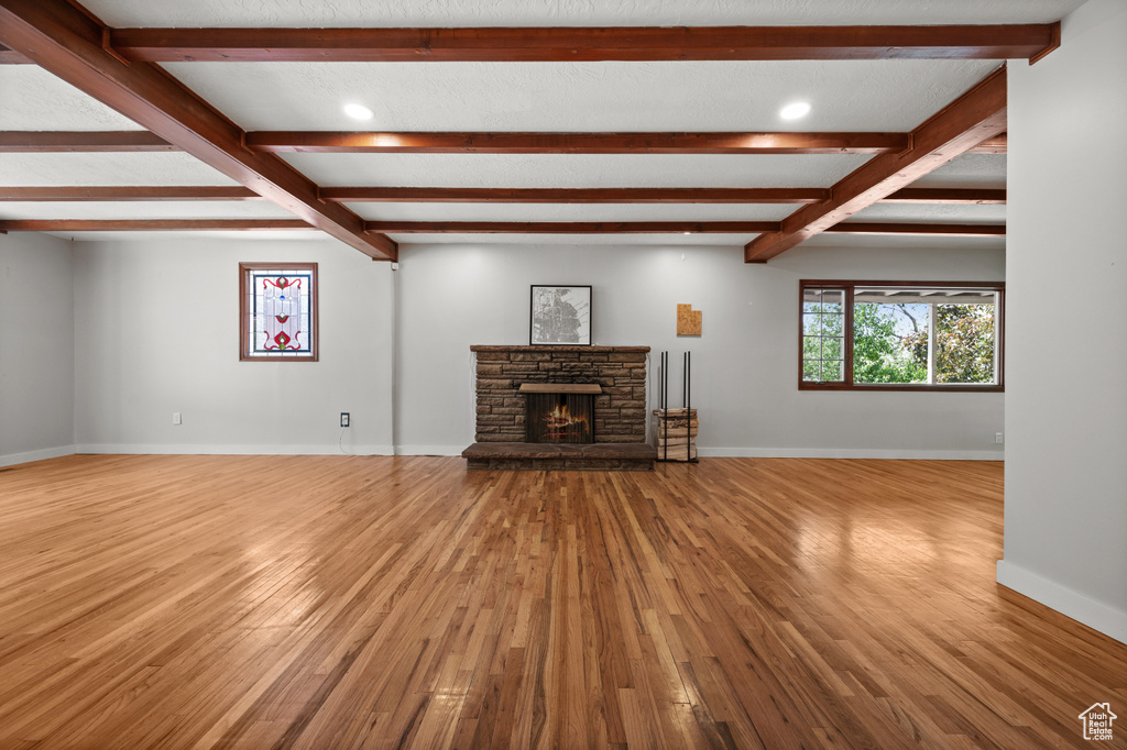 Unfurnished living room with wood finished floors, beam ceiling, baseboards, a fireplace, and recessed lighting