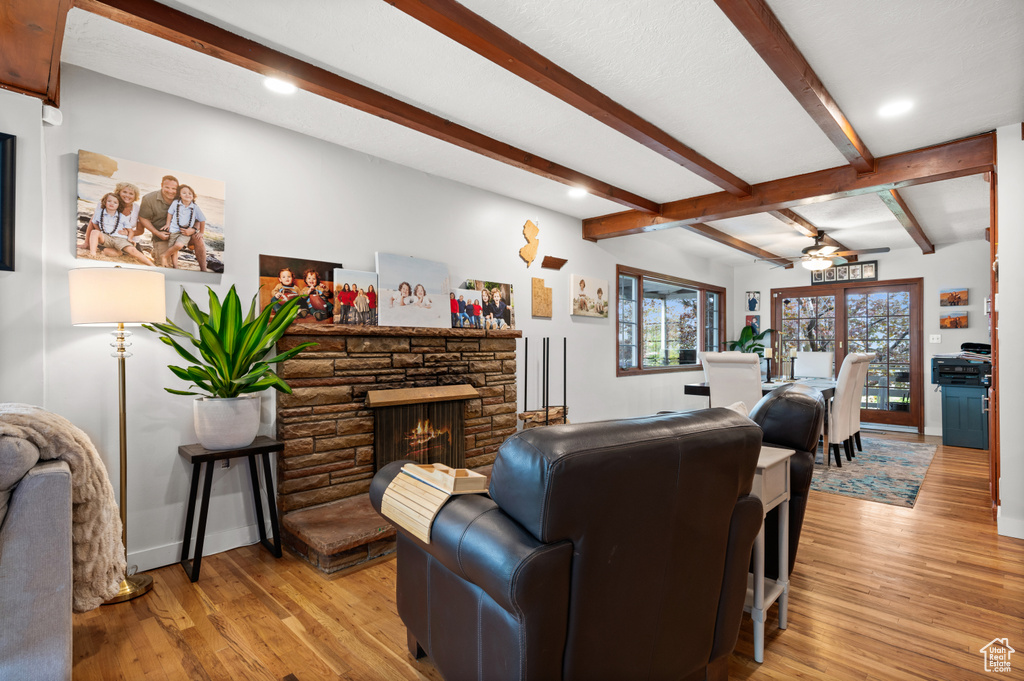 Living room with ceiling fan, a stone fireplace, baseboards, beamed ceiling, and light wood-style flooring