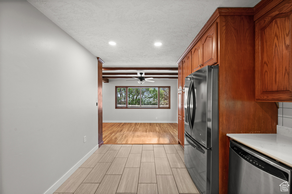 Kitchen with freestanding refrigerator, stainless steel dishwasher, wood finish floors, light countertops, and brown cabinets