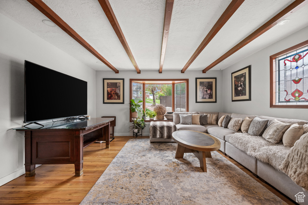 Living room with light wood-style floors, a textured ceiling, baseboards, and beam ceiling
