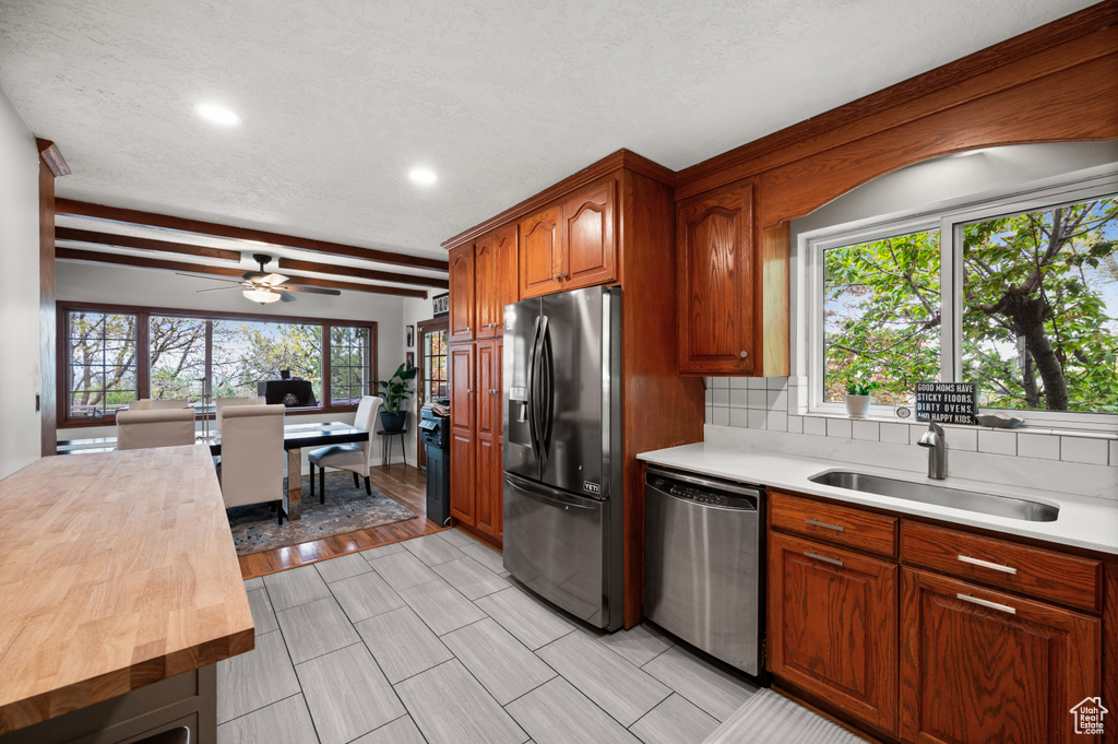 Kitchen with black refrigerator with ice dispenser, butcher block counters, a sink, dishwasher, and a wealth of natural light