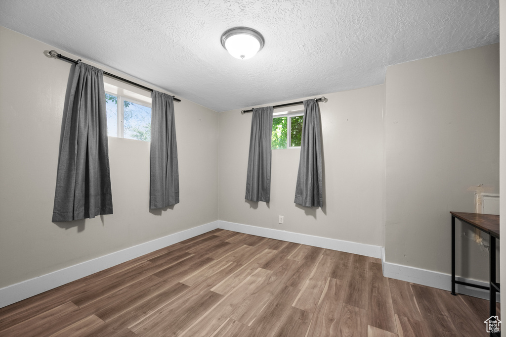 Unfurnished room with a textured ceiling, wood finished floors, and baseboards