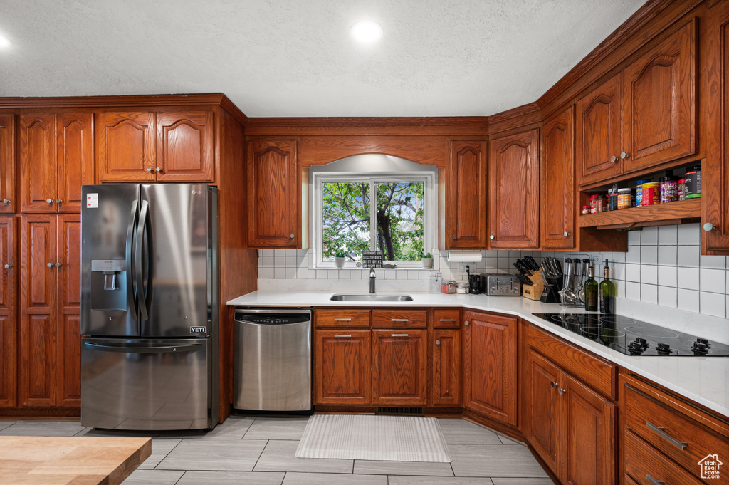 Kitchen featuring tasteful backsplash, dishwasher, a sink, fridge with ice dispenser, and black electric stovetop
