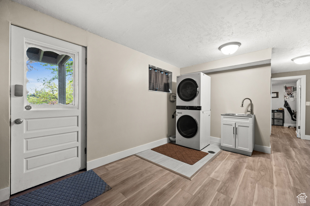 Clothes washing area featuring stacked washer and clothes dryer, baseboards, a textured ceiling, a sink, and light wood-style flooring