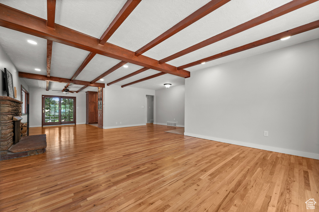 Unfurnished living room featuring light wood finished floors, beam ceiling, ceiling fan, a stone fireplace, and recessed lighting