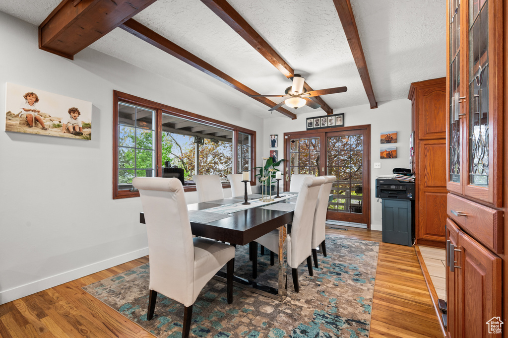 Dining room with beam ceiling, light wood finished floors, a textured ceiling, a ceiling fan, and baseboards