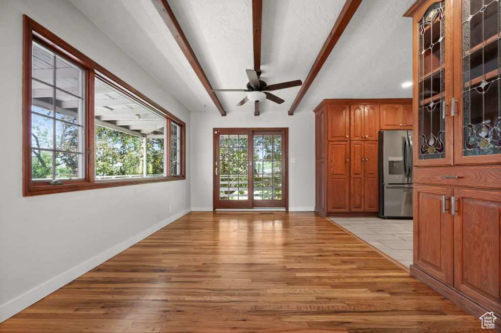Unfurnished dining area featuring beam ceiling, ceiling fan, light wood-style floors, baseboards, and a textured ceiling
