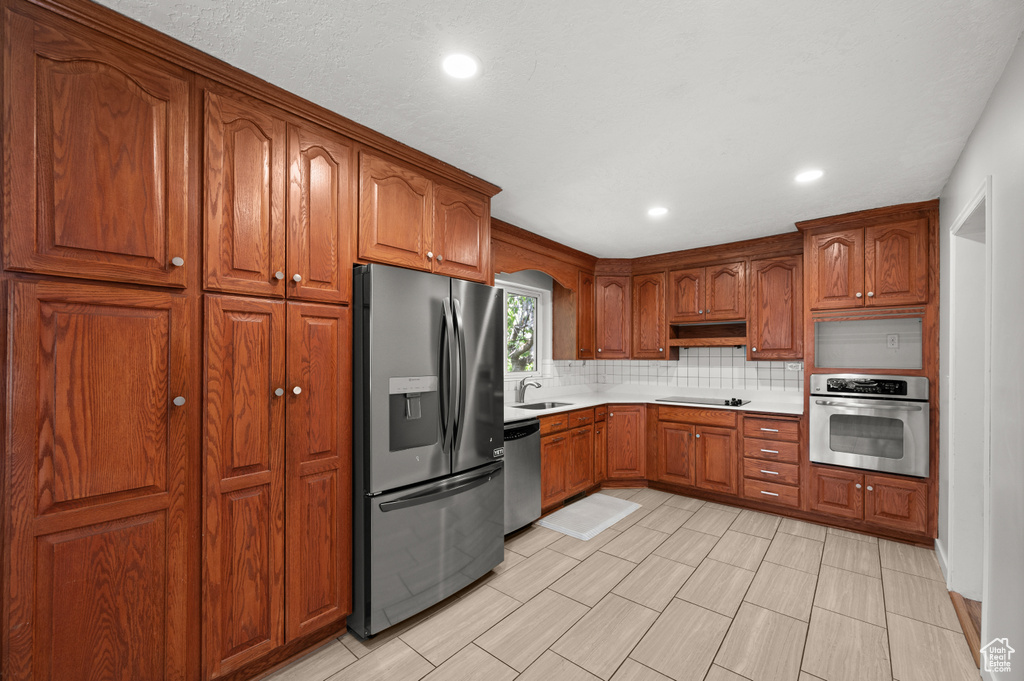 Kitchen with appliances with stainless steel finishes, tasteful backsplash, light countertops, recessed lighting, and brown cabinetry