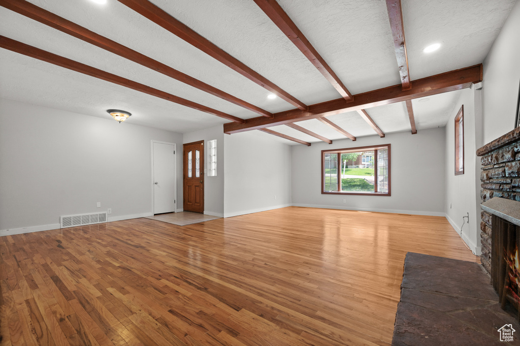 Unfurnished living room featuring a fireplace, light wood-type flooring, beam ceiling, baseboards, and recessed lighting