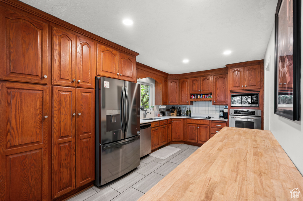 Kitchen featuring decorative backsplash, a sink, butcher block counters, stainless steel appliances, and recessed lighting