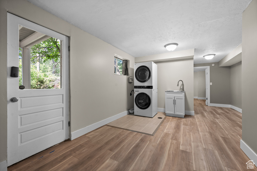 Washroom with cabinet space, stacked washing machine and dryer, light wood-style floors, baseboards, and a textured ceiling