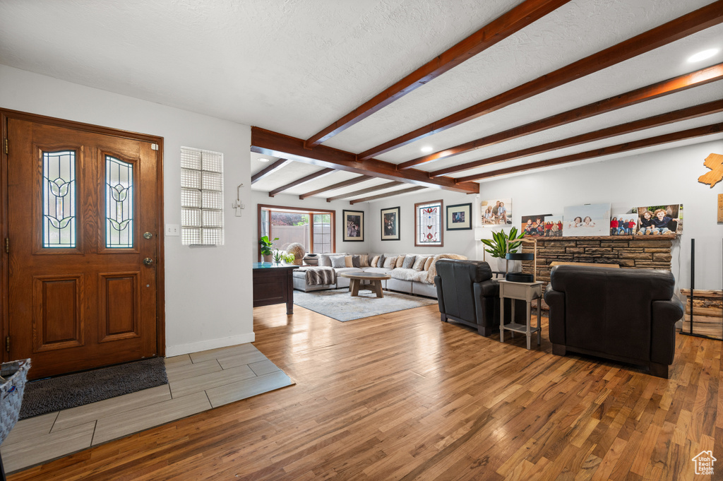 Foyer entrance with baseboards, a textured ceiling, beam ceiling, and wood finished floors