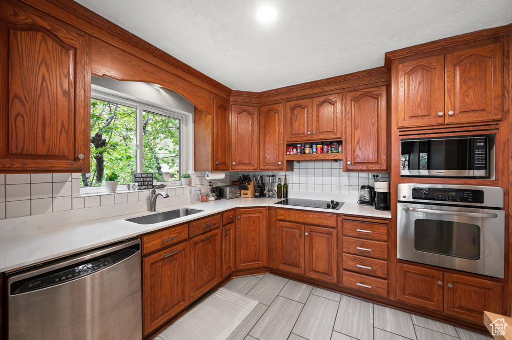 Kitchen with brown cabinetry, light countertops, a sink, backsplash, and stainless steel appliances