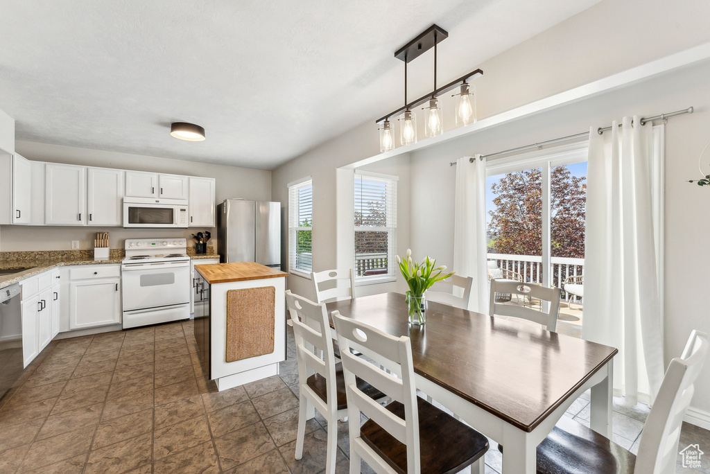 Kitchen with hanging light fixtures, baseboards, wood counters, white appliances, and white cabinetry