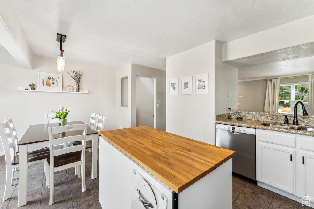 Kitchen with a sink, wood counters, white cabinetry, stainless steel dishwasher, and dark tile patterned floors
