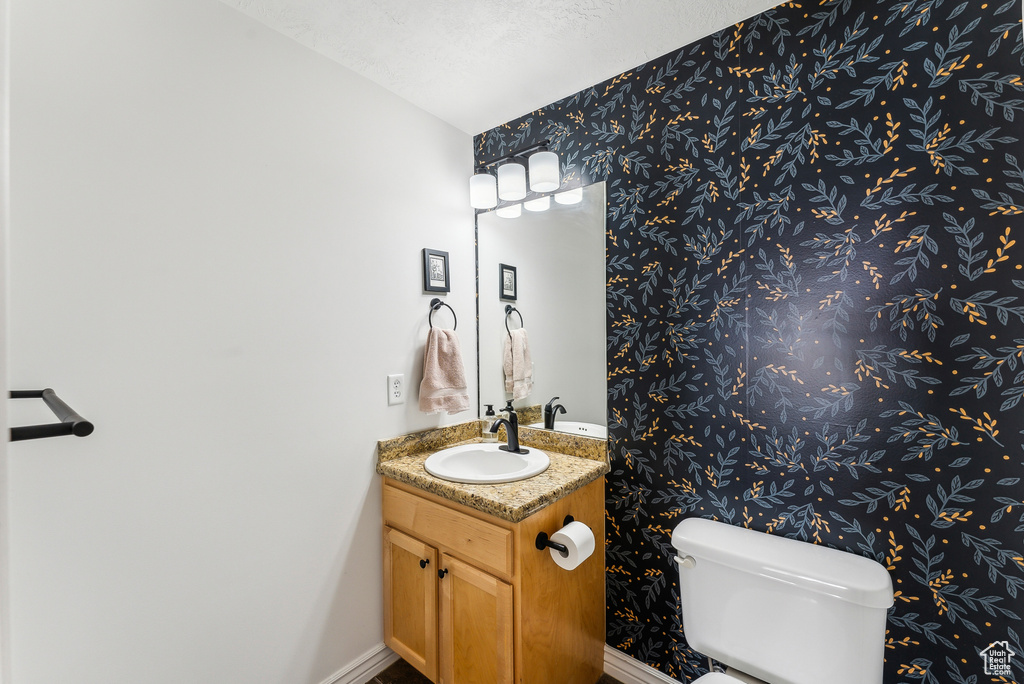 Half bathroom with vanity, baseboards, toilet, and wallpapered walls