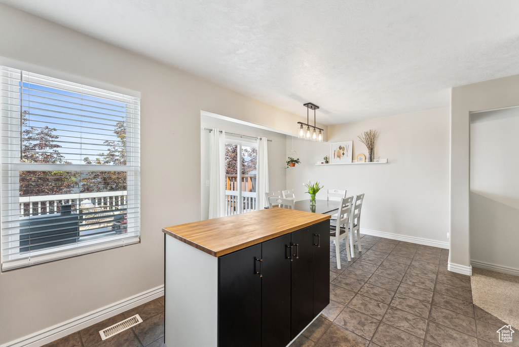 Kitchen featuring dark cabinets, butcher block countertops, decorative light fixtures, baseboards, and visible vents