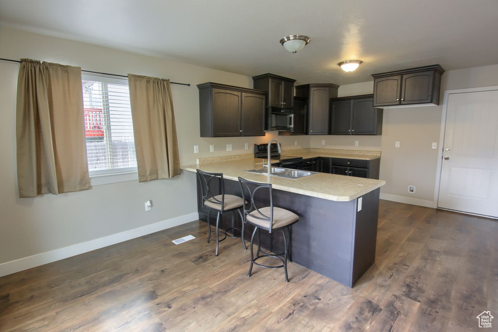 Kitchen featuring a kitchen breakfast bar, a sink, light countertops, baseboards, and a peninsula