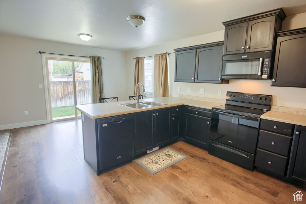 Kitchen with a peninsula, light countertops, a sink, light wood-style flooring, and black appliances