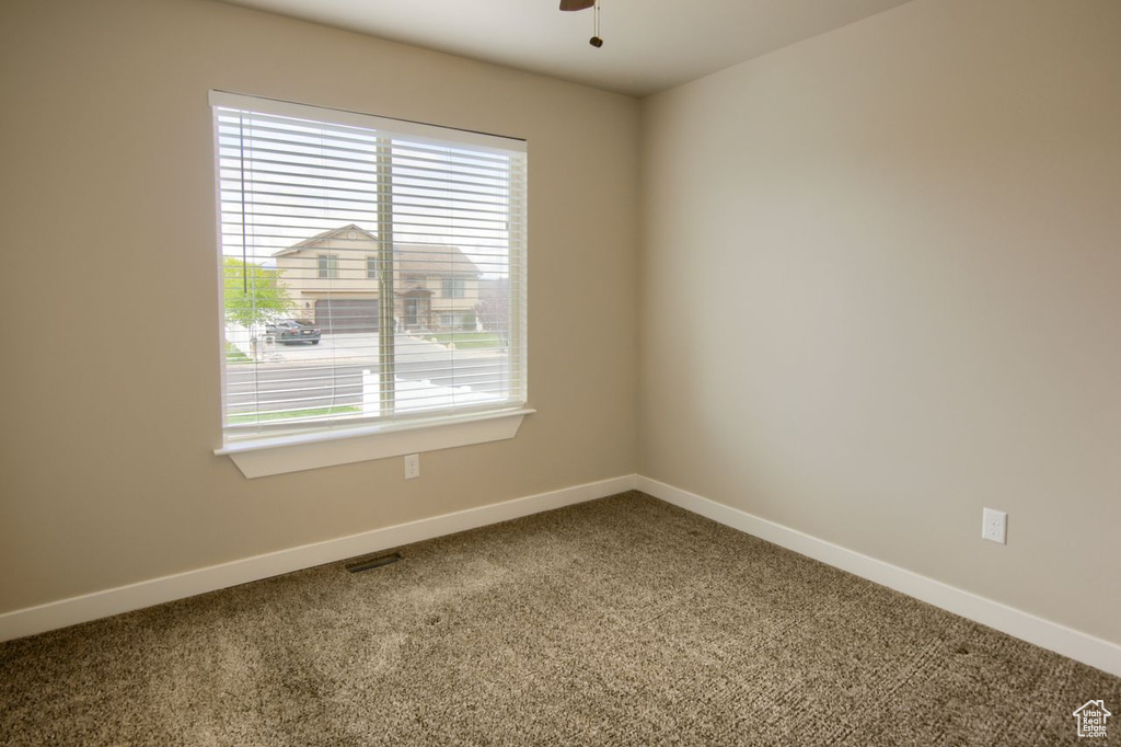 Carpeted empty room with baseboards, visible vents, and ceiling fan