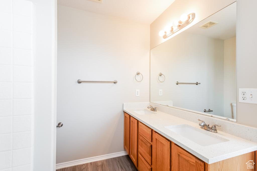 Bathroom featuring double vanity, wood finished floors, visible vents, and a sink
