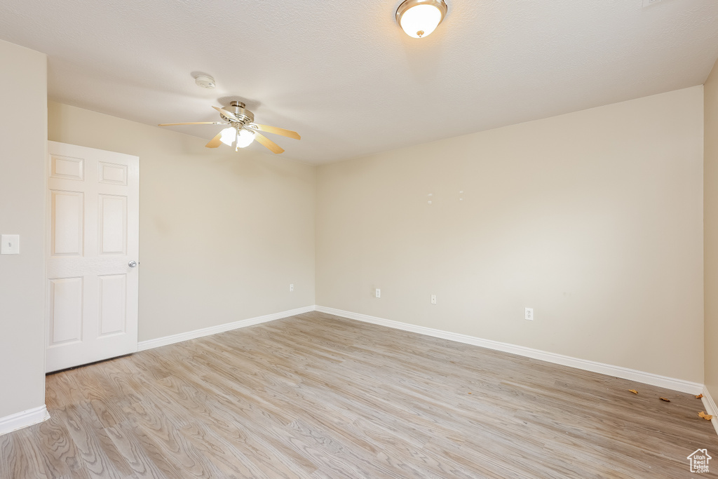Spare room with light wood finished floors, a ceiling fan, and baseboards