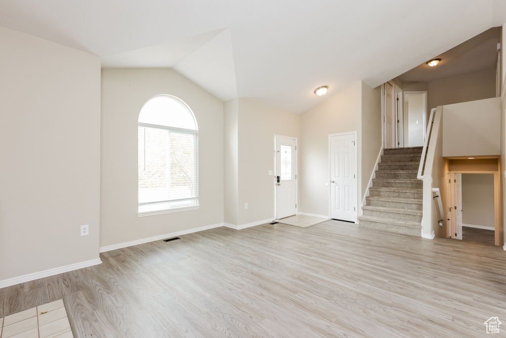 Unfurnished living room featuring light wood finished floors, stairway, lofted ceiling, and baseboards