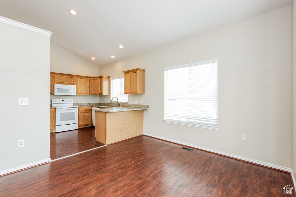 Kitchen with a sink, a peninsula, vaulted ceiling, white appliances, and dark wood finished floors