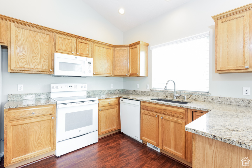 Kitchen featuring white appliances, light brown cabinets, vaulted ceiling, a sink, and dark wood-type flooring