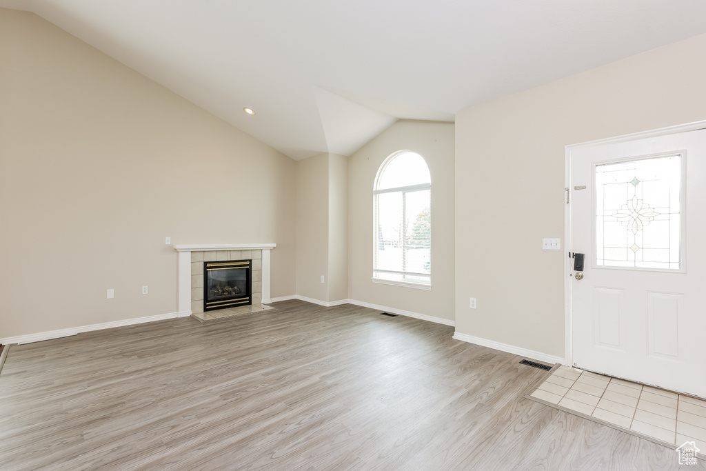 Unfurnished living room featuring light wood-style floors, a tiled fireplace, vaulted ceiling, and baseboards
