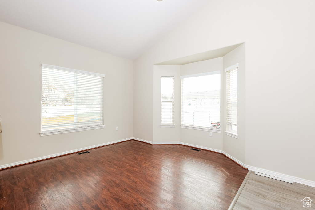 Spare room featuring wood finished floors, a healthy amount of sunlight, vaulted ceiling, and baseboards