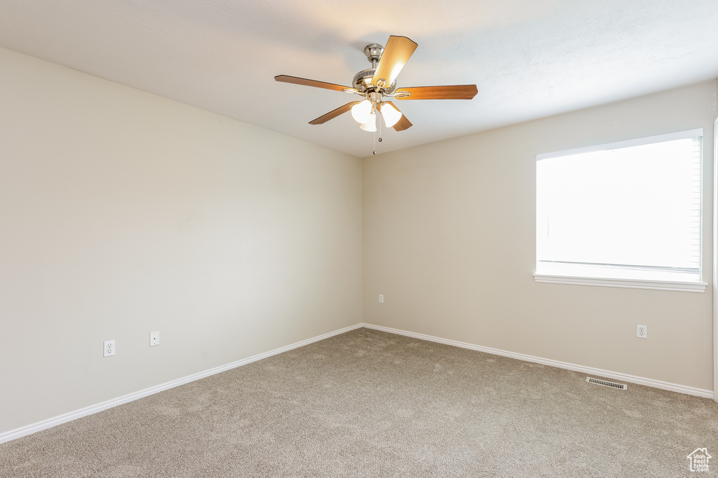 Carpeted empty room with visible vents, ceiling fan, and baseboards
