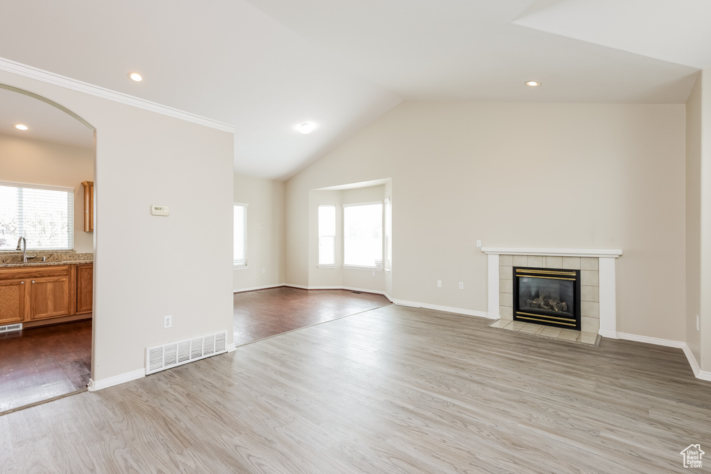 Unfurnished living room with wood finished floors, visible vents, a healthy amount of sunlight, and a tiled fireplace