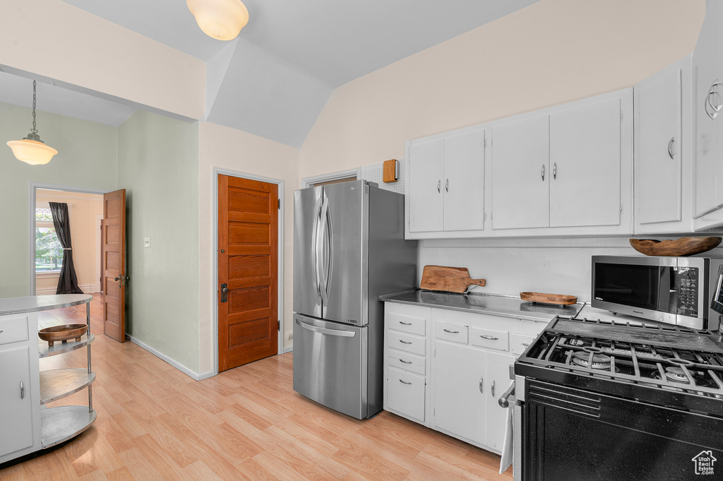 Kitchen with light wood-type flooring, white cabinets, appliances with stainless steel finishes, vaulted ceiling, and hanging light fixtures