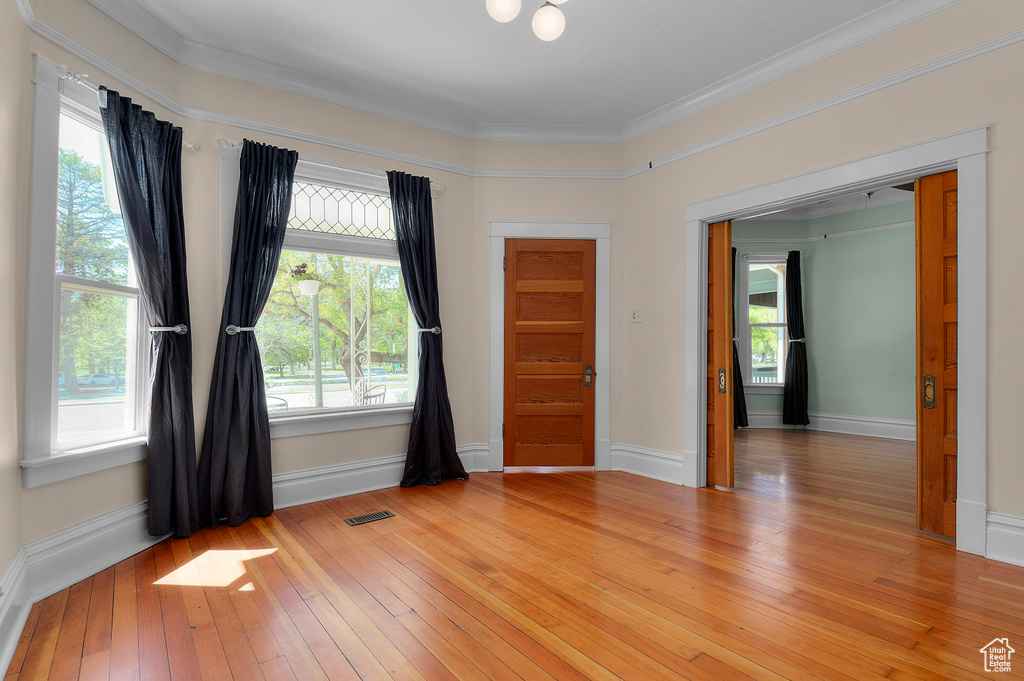 Spare room with crown molding, baseboards, visible vents, and light wood finished floors