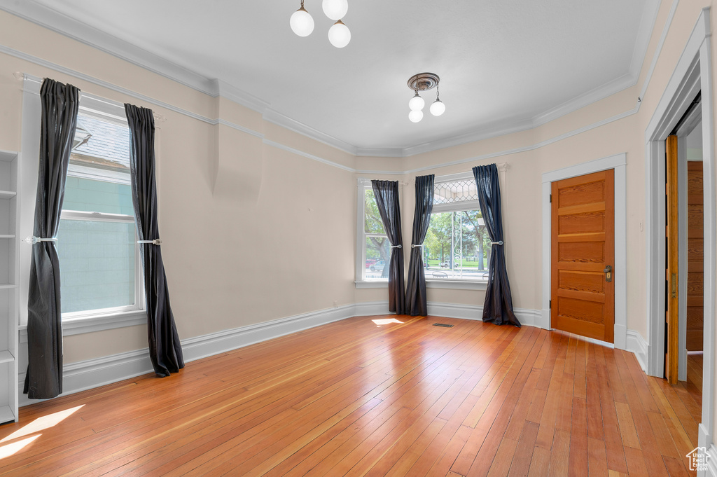 Unfurnished room with baseboards, ornamental molding, light wood-type flooring, and a chandelier