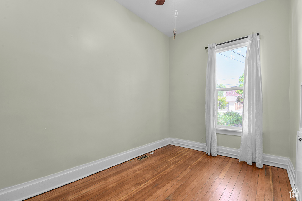 Empty room with a healthy amount of sunlight, baseboards, wood-type flooring, and a ceiling fan
