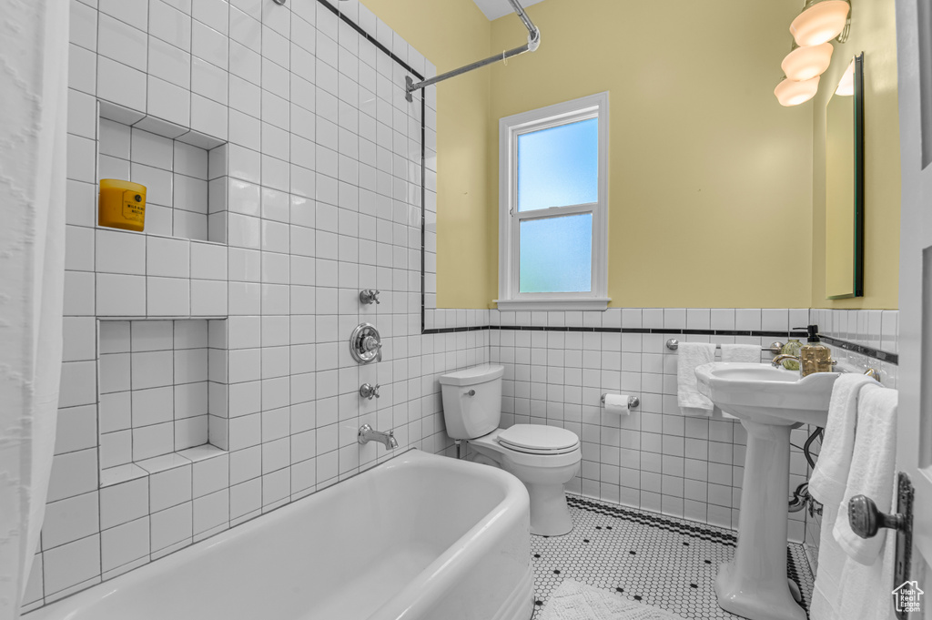 Full bathroom featuring tile patterned flooring, wainscoting, shower / bath combination with curtain, toilet, and tile walls