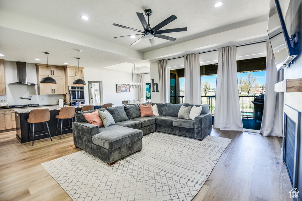 Living area featuring light wood-type flooring, recessed lighting, ceiling fan with notable chandelier, and a fireplace
