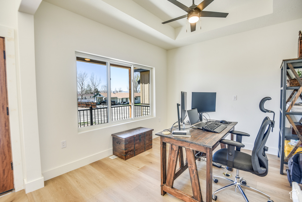 Office area featuring ceiling fan, a raised ceiling, arched walkways, baseboards, and light wood-type flooring