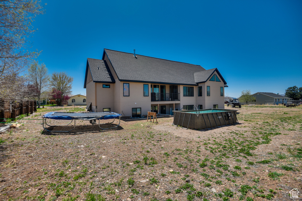 Rear view of property with roof with shingles, a fenced in pool, a trampoline, and a balcony