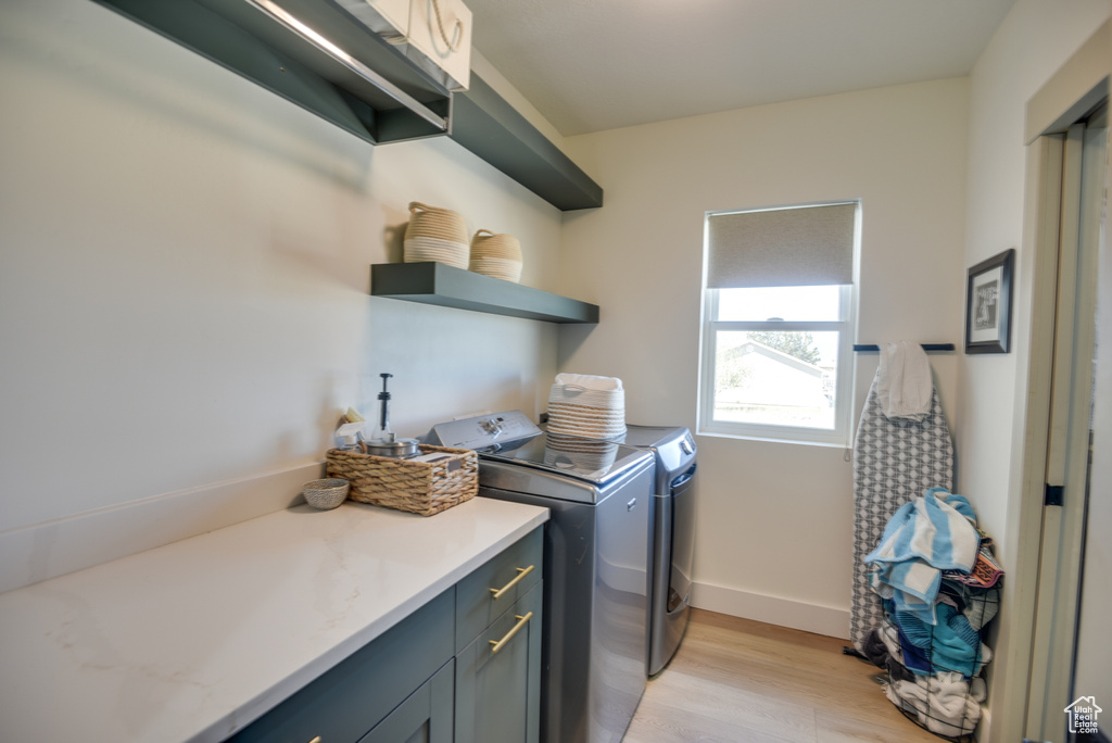 Laundry room with baseboards, light wood finished floors, cabinet space, and washing machine and clothes dryer