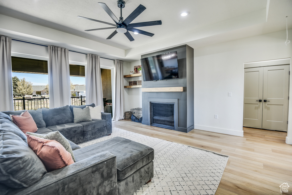 Living area featuring ceiling fan, a large fireplace, baseboards, and light wood-type flooring