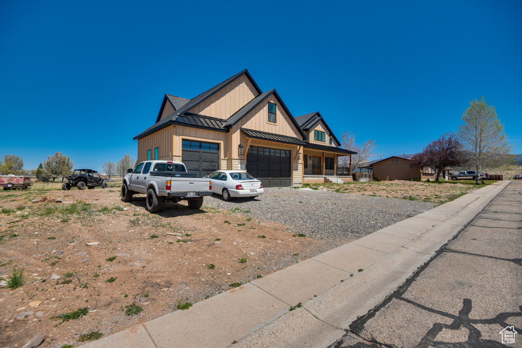 View of front of house with an attached garage, board and batten siding, a standing seam roof, driveway, and metal roof