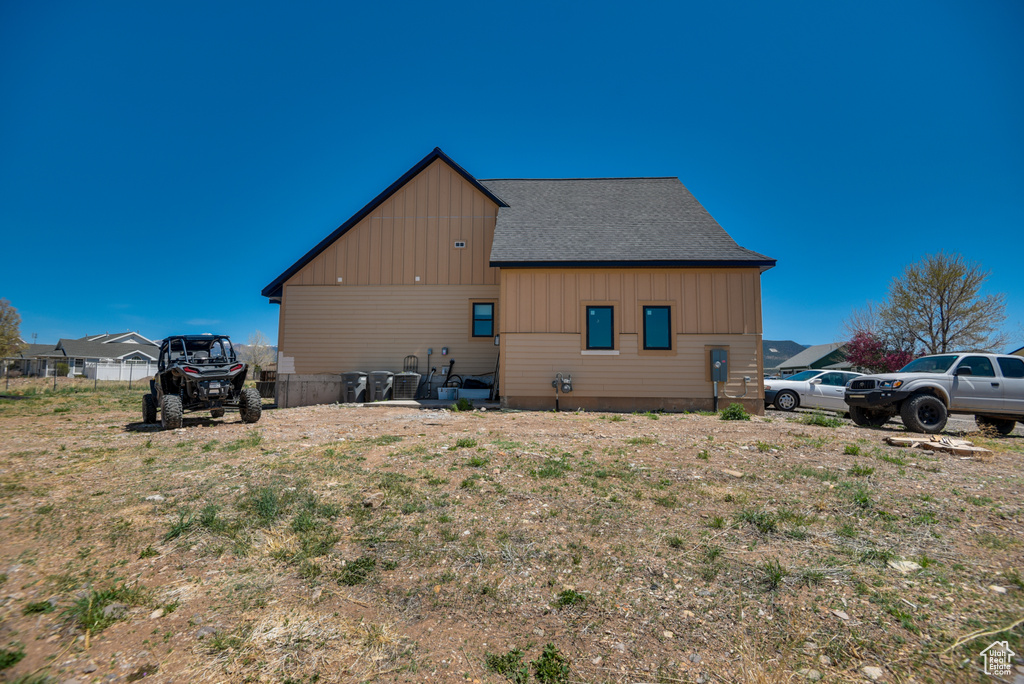 View of side of home with a shingled roof, board and batten siding, and fence
