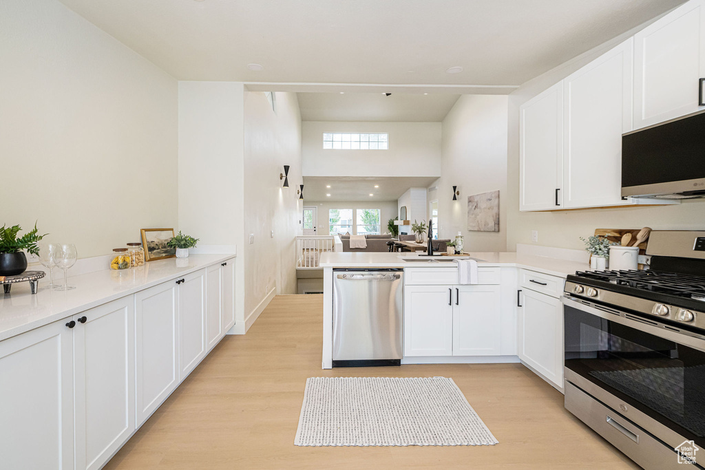 Kitchen featuring white cabinets, light wood finished floors, stainless steel appliances, and a peninsula